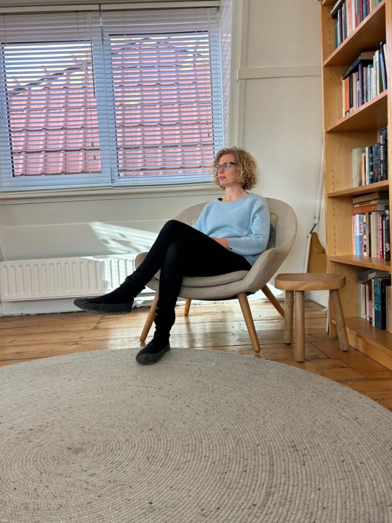 Eltica zit tijdens een gesprek in de praktijkruimte, naast het raam en de boekenkast.